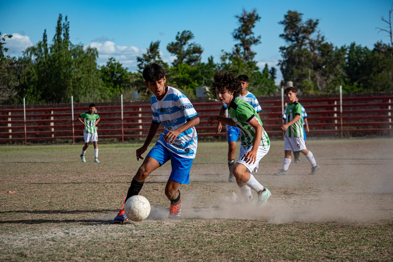 Teenage boys playing soccer on a sunny outdoor field, competing intensely.