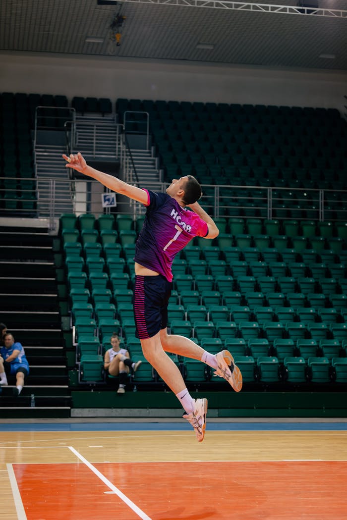 services-02 Dynamic image of a male volleyball player executing a high jump serve in an indoor arena.