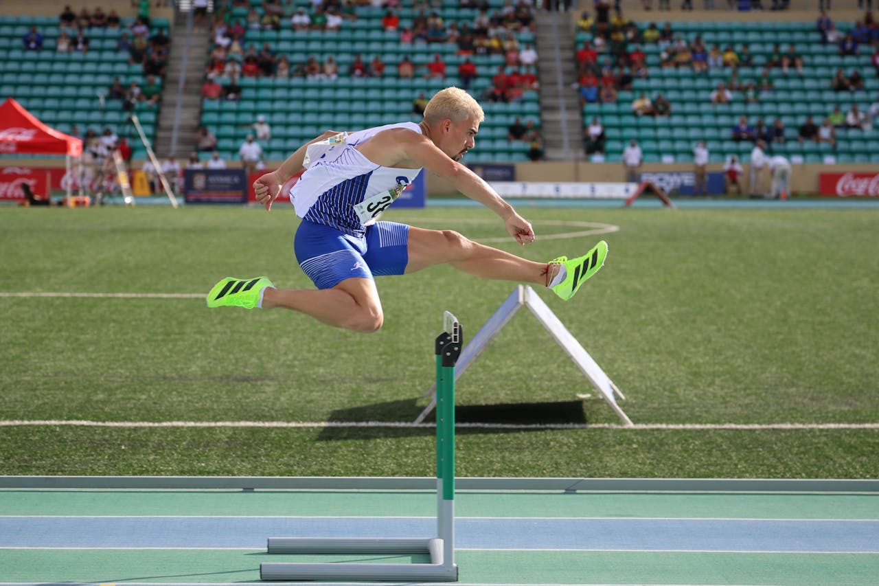 services-04 Dynamic shot of an athlete clearing a hurdle during an outdoor track event.